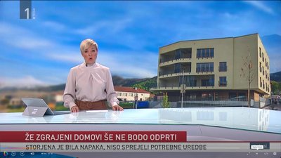Slika ženske z blond lasmi (voditeljice na TV SLO), v ozadju na sliki zgradba in napis (naslov) prispevka: Že zgrajeni domovi še ne bodo odprti. Storjena je bila napaka, niso sprejeli potrebne uredbe.